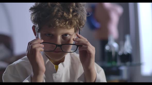 Close-up of Cute Caucasian Boy with Curly Hair Taking Off and Putting on Eyeglasses. Clever Teenager