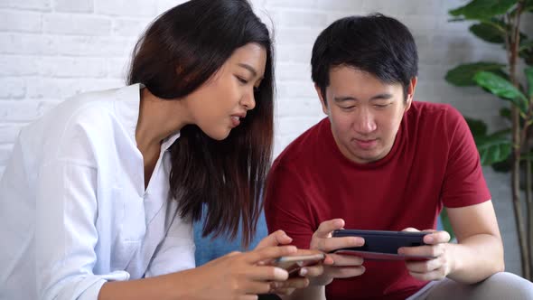Asian Man and Woman Using Smartphone to Play Videogame Together on Mobile Phone at Home