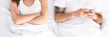 Woman With Arms Crossed Lying In Bed, Man Using Phone