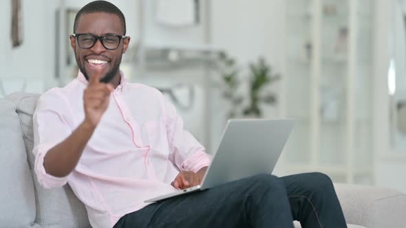 Excited African Man with Laptop Pointing at the Camera at Home