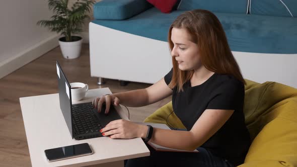 Young Woman Is Drinking a Cup of Coffee While Is Working at the Laptop From Home Office