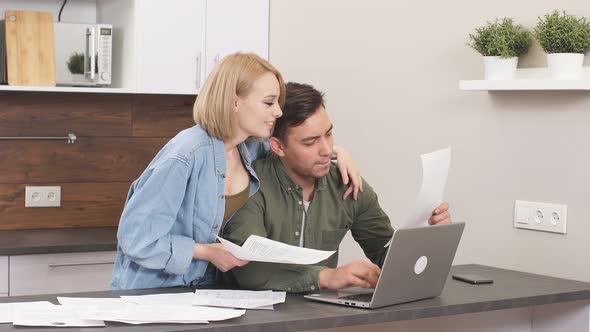 Positive Funny Married Couple Checking Finance at Home Using Laptop