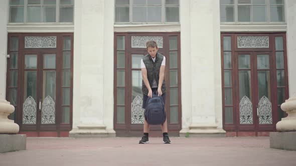 Wide Shot of Joyful Schoolboy Spinning with Rucksack After Classes Outdoors. Portrait of Happy