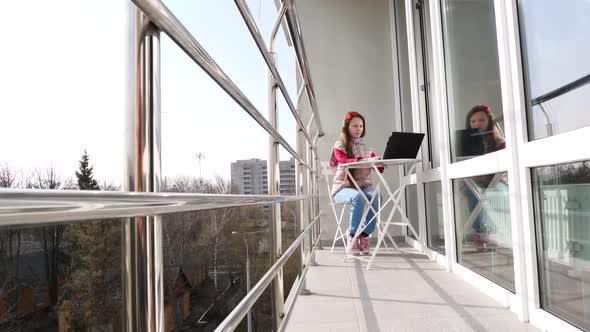 Pretty Teenager Girl Is Typing, Working on Laptop, on Open Balcony. Spring Sunny Day. Concept of