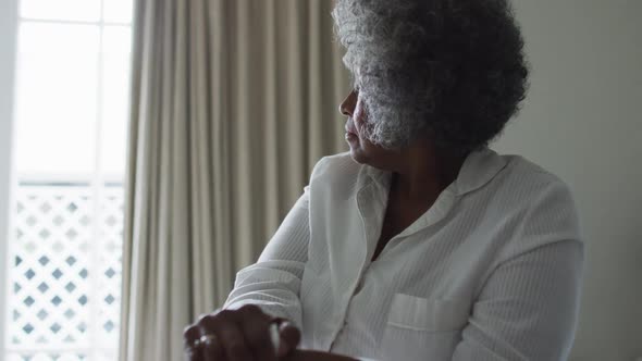 Senior african american woman holding walking stick sitting on the bed at home