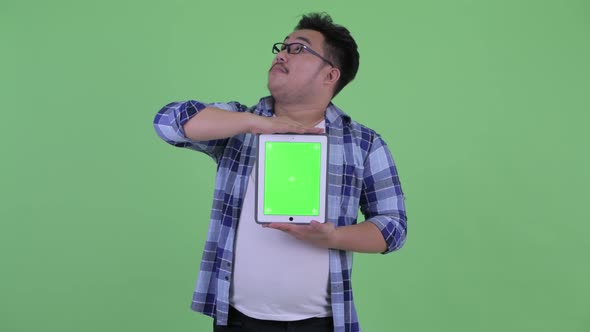 Happy Young Overweight Asian Hipster Man Thinking While Showing Digital Tablet