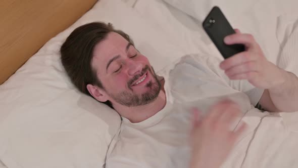 Casual Young Man Having Loss on Smartphone in Bed