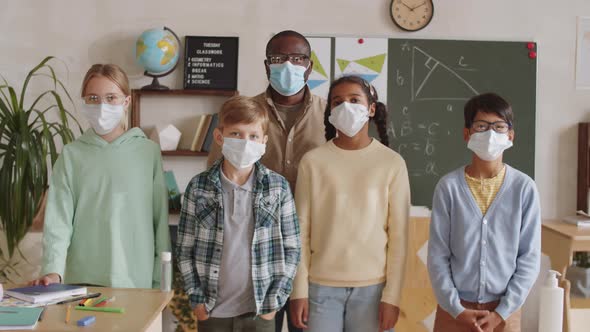 Teacher and Schoolkids in Face Masks Posing for Camera in Classroom