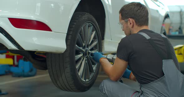 Mechanic Is Unscrewing Lug Nuts with a Pneumatic Impact Wrench, Specialists Removes the Wheel 