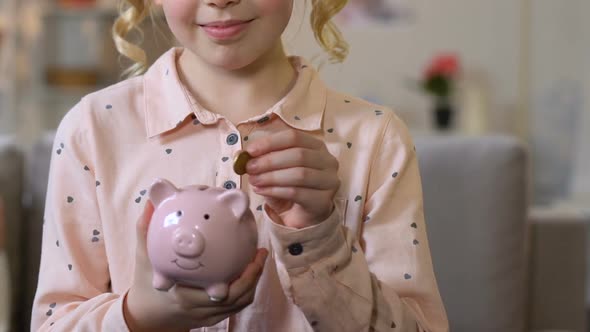 Adorable Girl Putting Coin Into Piggy Bank, Funds From Early Childhood, Closeup