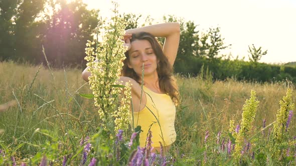 Pretty Young Girl is Sitting in the Middle of the Field with Flowers During Summer Time