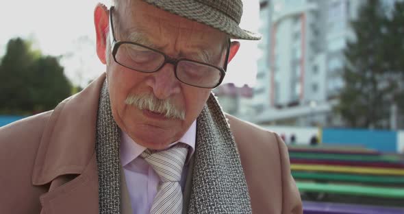 Close Portrait of Old Lonely Grandfather Reading on Bench Outdoors