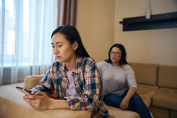 Despondent daughter using mobile phone during quarrel with parent