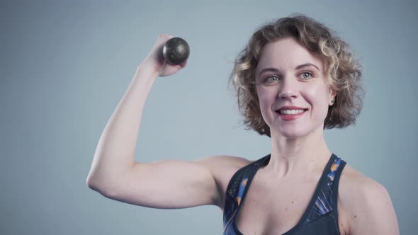 Sporty Female with Dumbbells Posing in Gym Against a Gray Wall