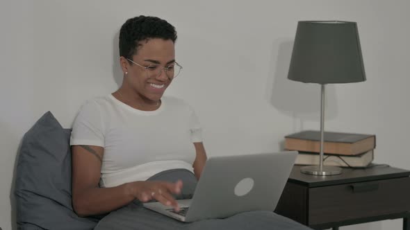 African Woman Celebrating Success on Laptop in Bed