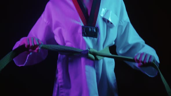 A Little Boy Doing Taekwondo in Neon Lighting  Tying Up His Green Belt and Waving His Hand