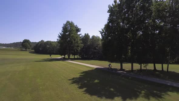 Man Mountain Bike Ride Outdoor in Nature Down a Side Walk in Sunny Day Aerial Drone Follow Wide Shot