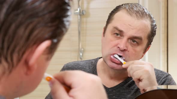  man brushes teeth looking in mirror in bathroom