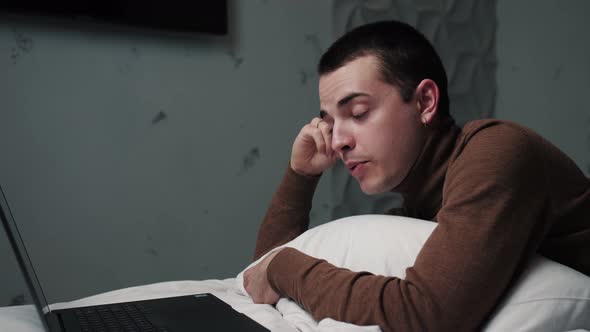 Caucasian Man Sitting on His Bed While Doing a Video Call Chatting From His Laptop. He Is Laughing