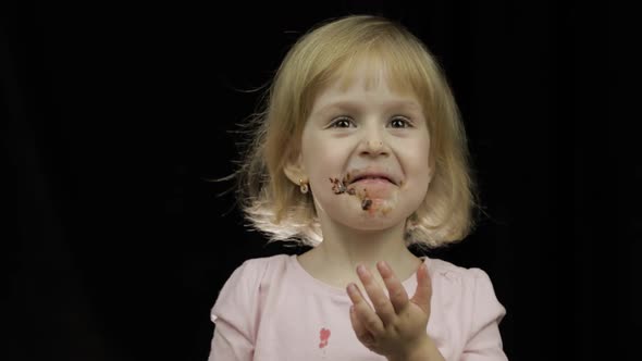 Child with Dirty Face From Melted Chocolate and Whipped Cream Eats Strawberry