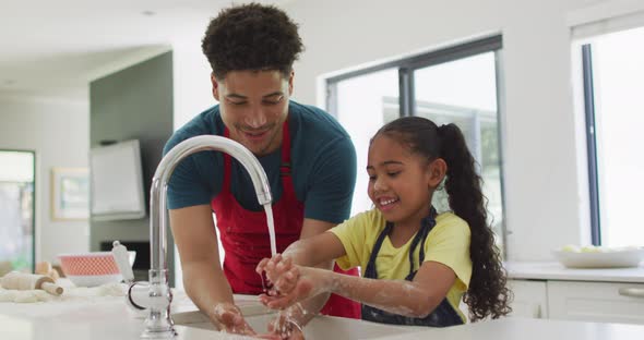 Happy biracial father and daughter washing hands in kitchen