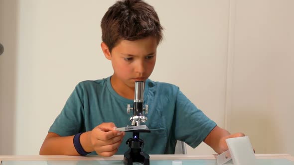 A Tanned Boy Is Looking at Object Glasses Through a Microscope