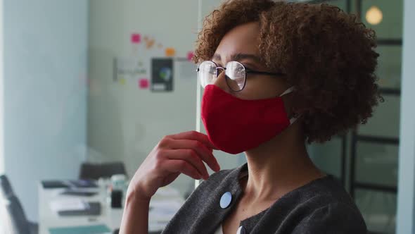 Thoughtful african american woman wearing face mask with hand on chin at modern office