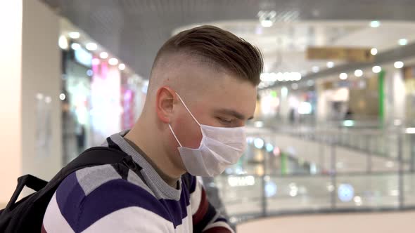 A Young Man in a Medical Mask on the Second Floor in a Shopping Center, The Man Is Coughing