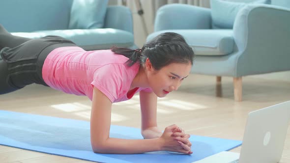Asian Woman Doing Yoga Plank And Watching Online Tutorials On Laptop, Training In Living Room