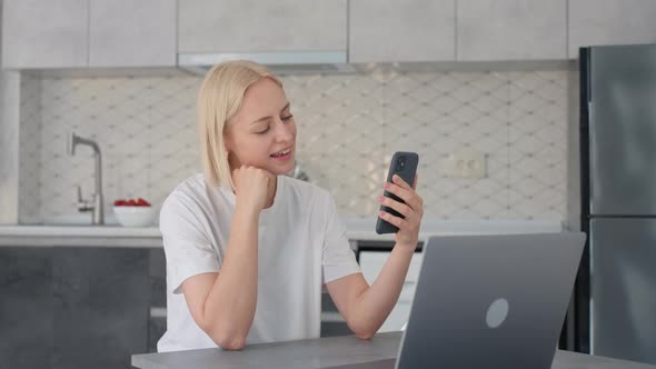 Joyful Blonde Woman Waves Bye in Video Call When Sitting at Laptop in Kitchen