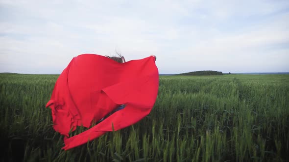 Young Girl Running with Red Tissue in Green Field. Happy Cute Girl Playing in the Wheat Field on a