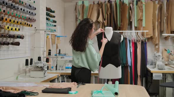 seamstress is measuring clothing on tailoring dummy with measure-tape. Woman is concentrated