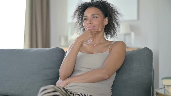 Pensive African Woman Sitting on Sofa and Thinking at Home