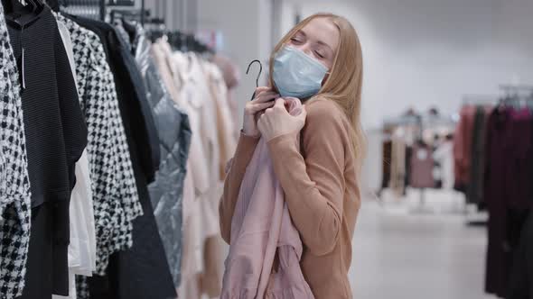 Blonde Caucasian Girl Woman Shopper in Medical Mask Chooses Perfect Casual Blouse Finds Clothes