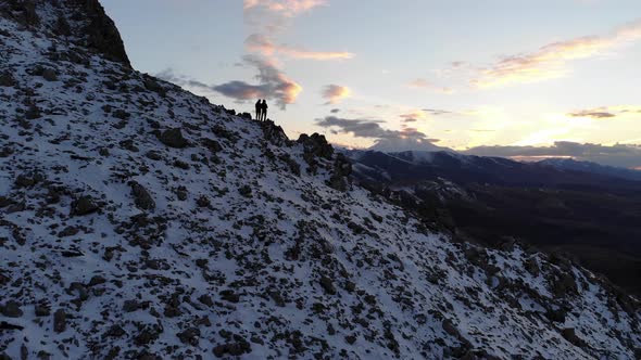 Aerial View of a Young Couple of Athletes Travelers Stands in the Mountains at Sunset in an Embrace