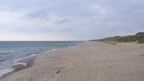 AERIAL: Slowly Flying Over Sandy Beach with Lots of Foot Prints on the Ground and Cloudy Sky