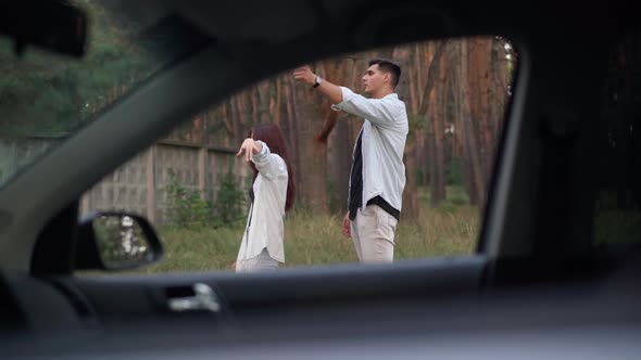 Young Man and Woman Gesturing Hitchhiking Standing at Broken Automobile Outdoors