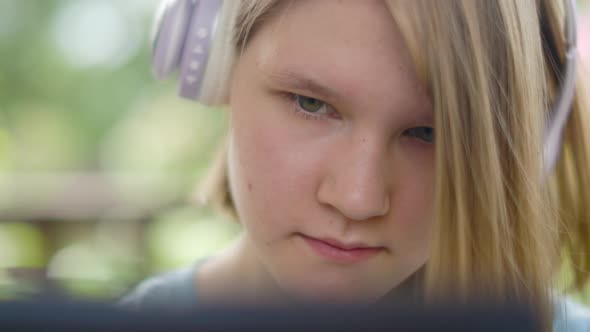 Teenage Girl Sits At Wooden Table In a Summer Cafe In Headphones With Phone