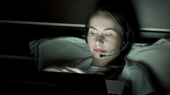 Young Woman Using Laptop Headset Working From Home Video Call in Bedroom at Night