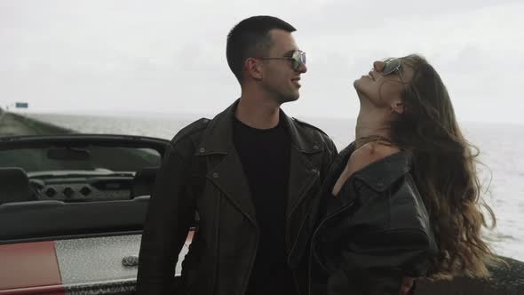 Young Couple Stand Near the Sea and Their Cabriolet