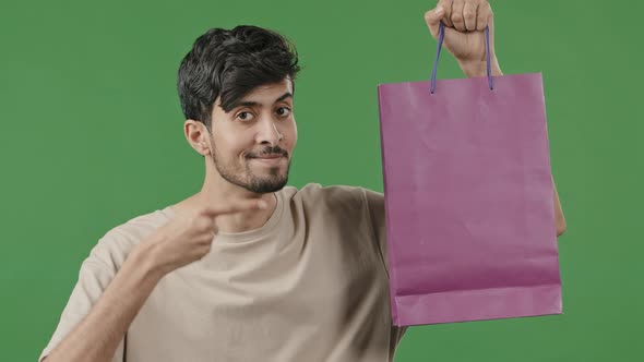 Happy Hispanic Guy Hold Shopping Bag Posing in Studio Smiling Young Arabic Man Points to Package