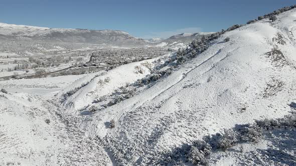 Slow aerial flight over a hillside toward the town of Eagle with fresh snow in December. Filmed in t