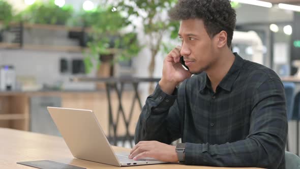 African American Man with Laptop Talking on Smartphone