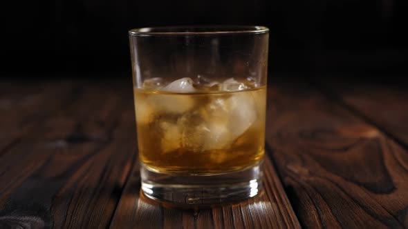 Closeup of a Woman Twirling a Glass of Whiskey with Ice on a Wooden Background