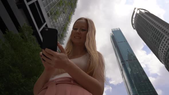 Superslowmotion Shot of a Young Woman Thar Use a Smartphone in Downtown Area with Skyscrapers at a