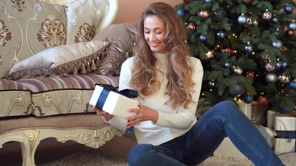 Christmas. Woman Dressed White Sweater and Jeans Sitting on the Floor Near Christmas Tree with