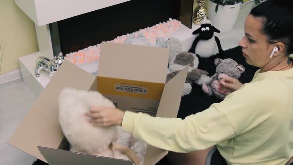 Woman takes out soft toys from a cardboard box while sitting on the floor. Close-up unpacking