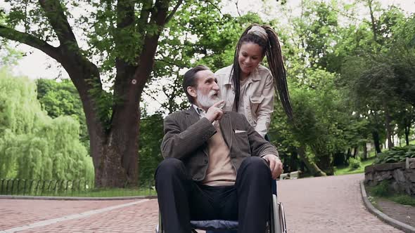 Trendy Grandaughter and Her Bearded Sedentary Bearded Granddad in Wheelchair Having Fun Together 