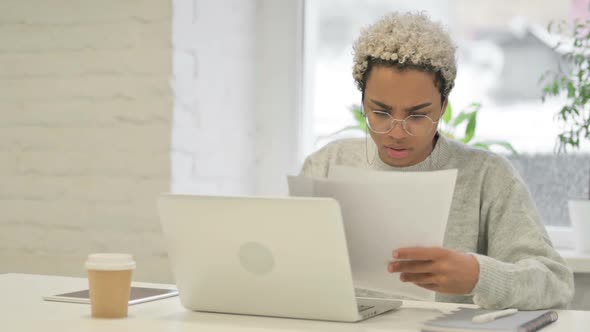 African Woman with Laptop Upset While Reading Documents in Office