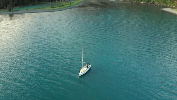 White Sailboat Floating On Calm Lake With Forest On Mountain In Alaska. - aerial